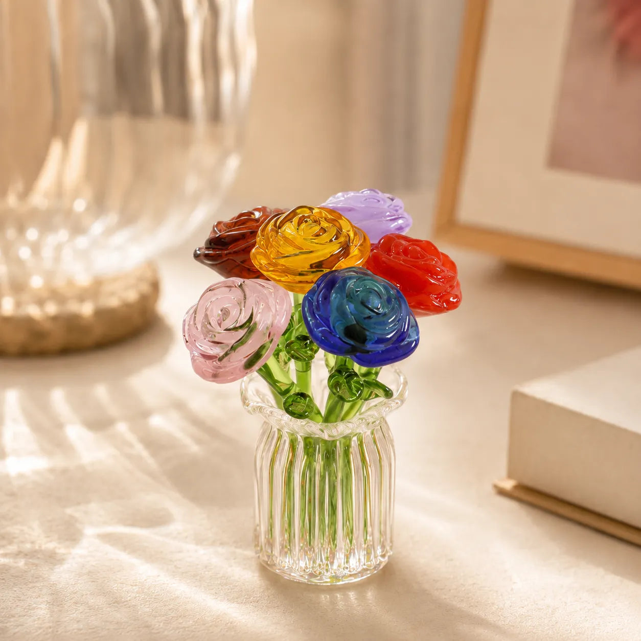 Colorful glass flowers in a clear vase on a light surface with a blurred background